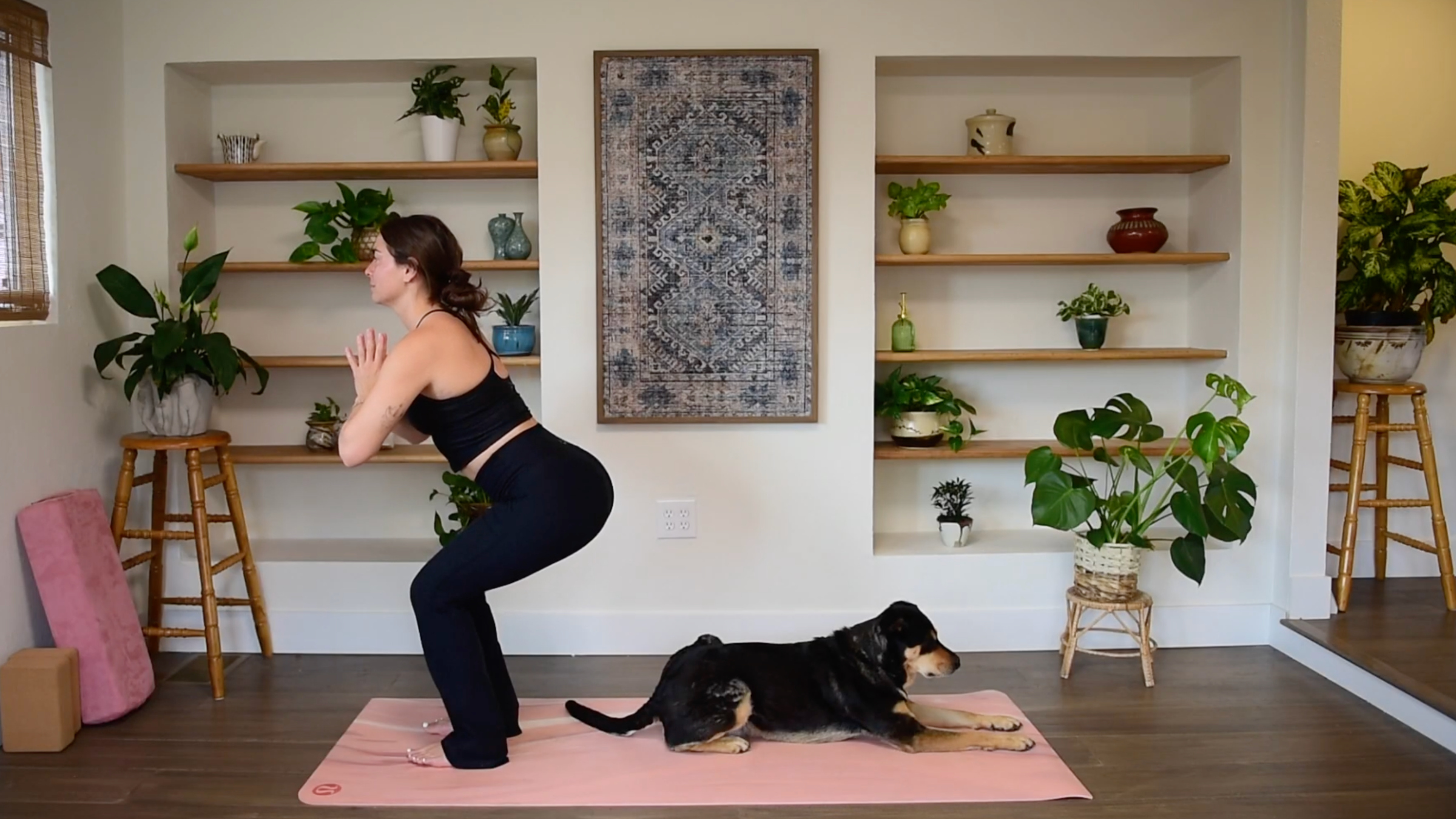 Caitlin K'eli sinking her hips into a squat with knees bent and hands in prayer position at the chest in Chair Pose.